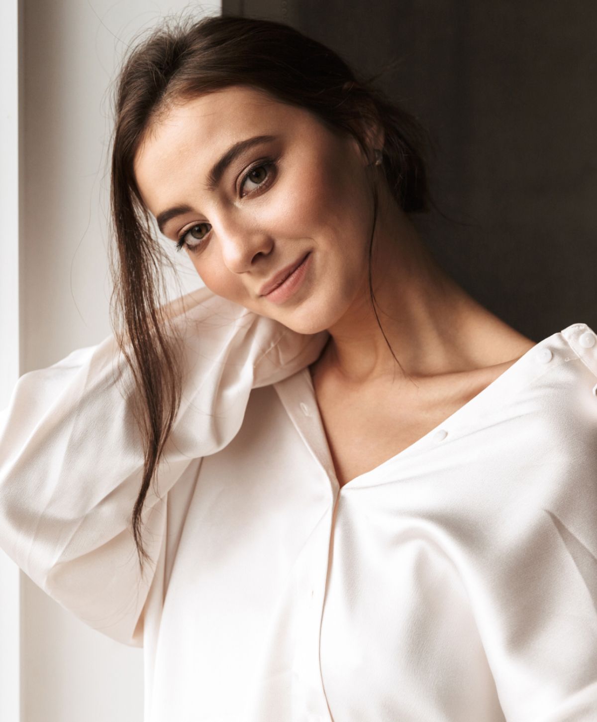 Model posing by window in neutral attire.